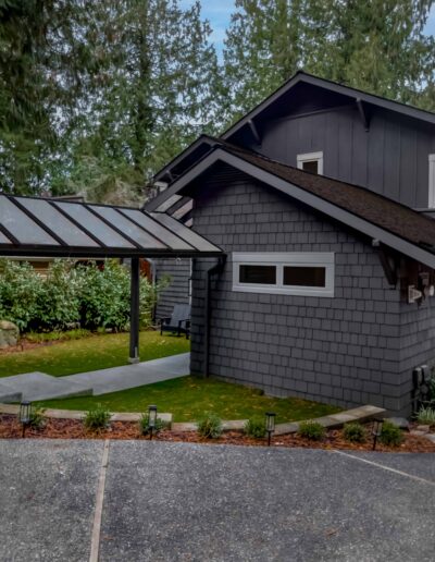 Two-story dark gray house with shingle siding, outdoor walkway, and covered entry, surrounded by trees and landscaping.