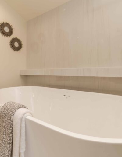 Modern bathroom with a white freestanding bathtub, a floor-mounted black faucet, and two towels draped over the tub; decorative wall art is visible.